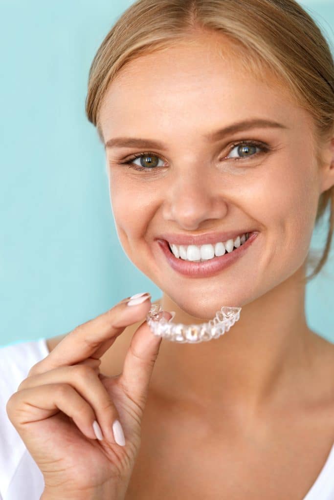 Smiling female patient holding Invisalign braces